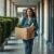 Employee walking out of office building holding a cardboard box after layoff.
